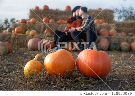 Couple sitting on hay bales in a pumpkin patch 118933089