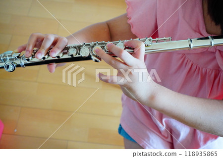 The hands of a fifth-grade girl practicing the flute indoors. 118935865