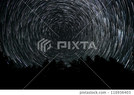 Star trails illuminate the night sky above a forested landscape showcasing celestial wonders in a remote area Star trails illuminate the night sky above a forested landscape showcasing celestial wonders in a remote area 118936403