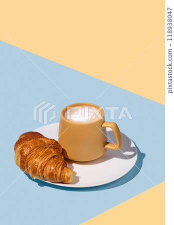 Coffee cup and fresh croissant on a white plate on a blue and yellow background. 118938047