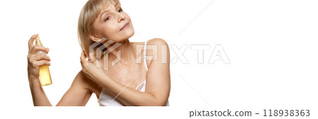 Banner. Mature woman with calm expression holds beauty spray against white studio background with negative space to insert text. 118938363