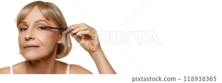 Banner. Woman applies mascara with precision, completing her makeup look against white background with negative space to insert your text. 118938365