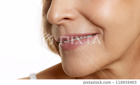 Radiant close-up of woman's smile, slightly turned to side, emphasizing natural beauty and smooth skin against white studio background. Radiant close-up of woman's smile, slightly turned to side, emphasizing natural beauty and smooth skin against white studio background. 118938403