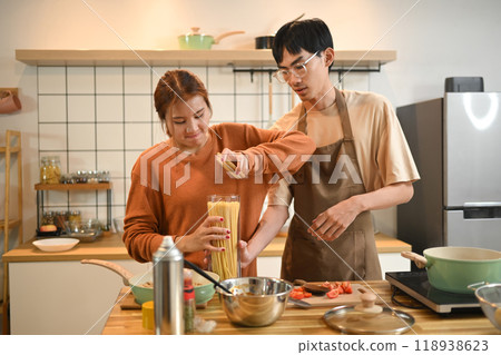Happy young couple preparing a meal together on wooden countertop filled with cooking ingredients Happy young couple preparing a meal together on wooden countertop filled with cooking ingredients 118938623