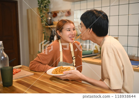 Lovely young couple eating pasta together, have fun in kitchen. People, food and relationships concept Lovely young couple eating pasta together, have fun in kitchen. People, food and relationships concept 118938644