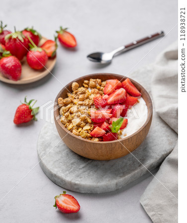 Natural yogurt with granola and strawberries in a wooden bowl on a marble board on light background Natural yogurt with granola and strawberries in a wooden bowl on a marble board on light background 118938721