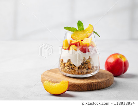 Yogurt parfait with peach and granola in a glass on a wooden board on a light background Yogurt parfait with peach and granola in a glass on a wooden board on a light background 118938954