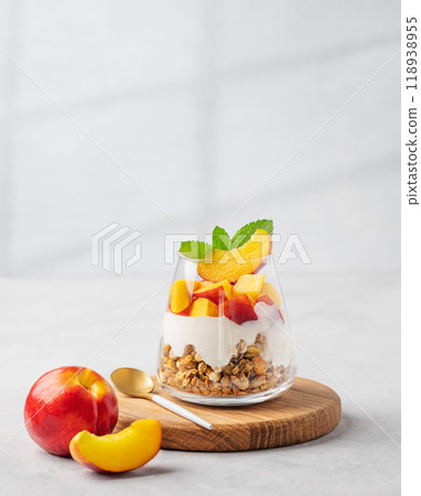 Yogurt parfait with peach and muesli in a glass on a wooden board on a light background Yogurt parfait with peach and muesli in a glass on a wooden board on a light background 118938955