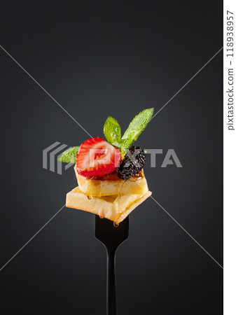 Wafer pieces with fresh strawberries, blackberries, mint leaves and dripping honey on a black fork Wafer pieces with fresh strawberries, blackberries, mint leaves and dripping honey on a black fork 118938957