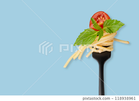 Spaghetti on a black fork with a piece of tomato, sauce and basil on a blue  background. 118938961