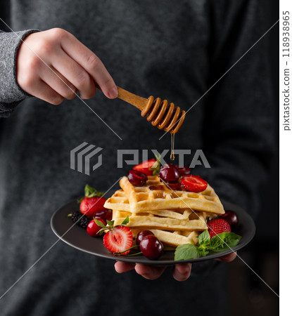 Hands holding a plate of Belgian waffles with fresh strawberries, blackberries, mint leaves  118938965
