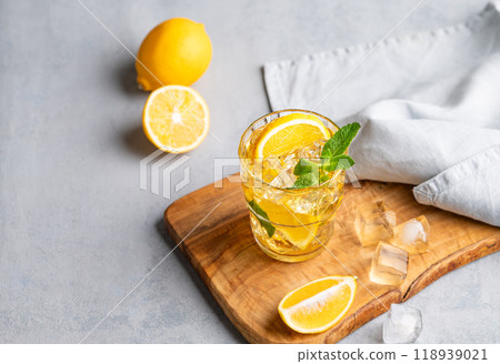 Iced drink with lemon, mint in a glass on a wooden board on a light background with citrus fruits. 118939021