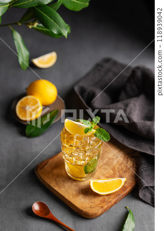 A glass of iced tea with lemon and mint on a wooden board on a dark background with citrus fruits A glass of iced tea with lemon and mint on a wooden board on a dark background with citrus fruits 118939042