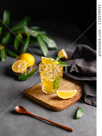 A glass of iced tea with lemon and mint on a wooden board on a dark background with citrus fruits 118939043