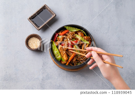 Stir-fry with soba noodles, meat and vegetables in black plate on a light background Stir-fry with soba noodles, meat and vegetables in black plate on a light background 118939045