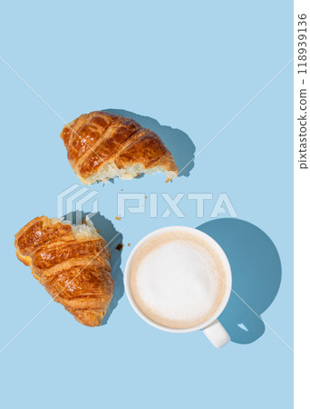 Flat lay of coffee cup and fresh broken croissant on blue background with shadow. Flat lay of coffee cup and fresh broken croissant on blue background with shadow. 118939136