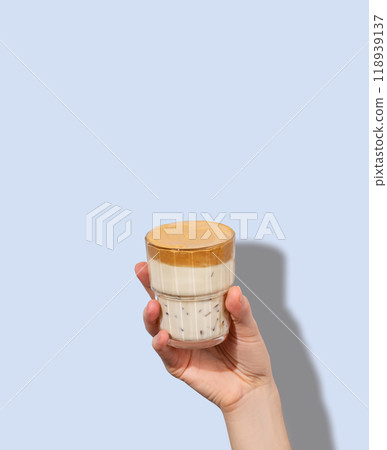 Dalgona coffee. A hand holds a glass of whipped and instant iced coffee and milk in a glass  118939137