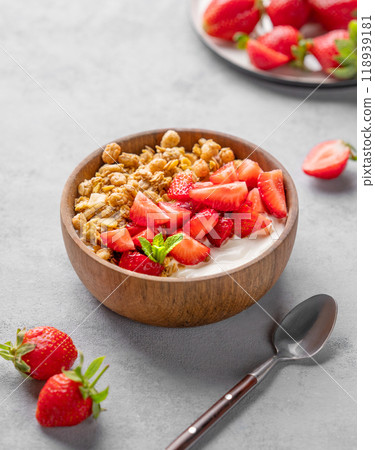 Natural yogurt with granola and strawberries in a wooden bowl on a blue background with berries. Natural yogurt with granola and strawberries in a wooden bowl on a blue background with berries. 118939181