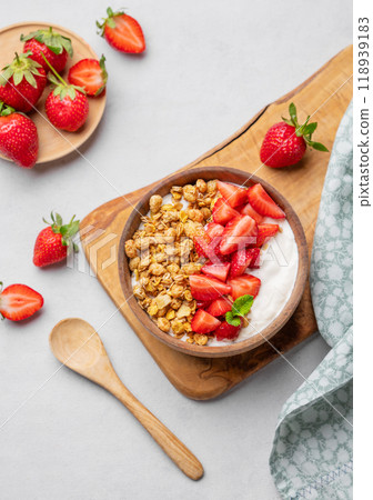 Natural yogurt with granola and strawberries in a wooden bowl on a wooden board on light background 118939183
