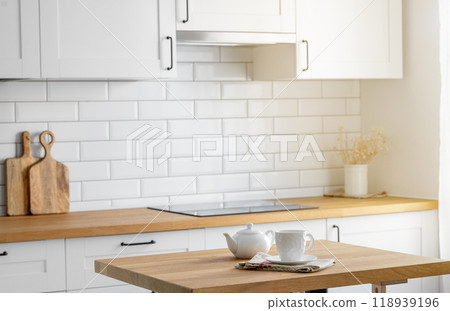 Wooden oak tabletop with a cup of tea and a kettle against the backdrop of a white kitchen Wooden oak tabletop with a cup of tea and a kettle against the backdrop of a white kitchen 118939196