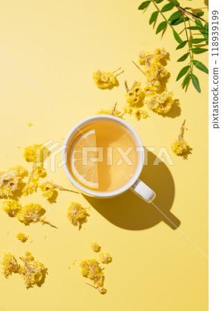 Herbal tea with immortelle and lemon in a white cup on a yellow background. 118939199