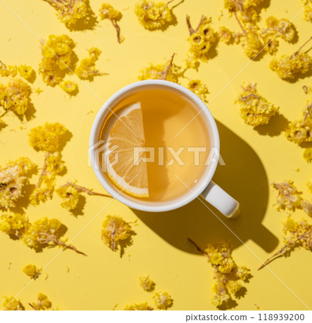 Herbal tea with immortelle and lemon in a white cup on a yellow background close up. 118939200