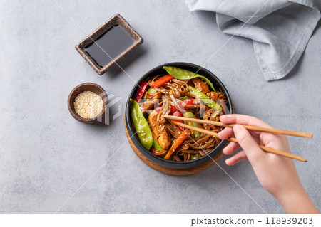 Stir-fry with soba noodles, meat and vegetables in black plate on a light background Stir-fry with soba noodles, meat and vegetables in black plate on a light background 118939203