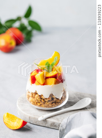 Yogurt parfait with peach and granola in a glass on a marble board on a light background  118939223