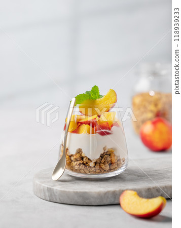Greek yogurt parfait with peach and muesli in a glass on a marble board on a light background Greek yogurt parfait with peach and muesli in a glass on a marble board on a light background 118939233
