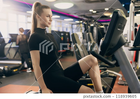 Young woman exercising on stationary bike in modern gym during daytime 118939605