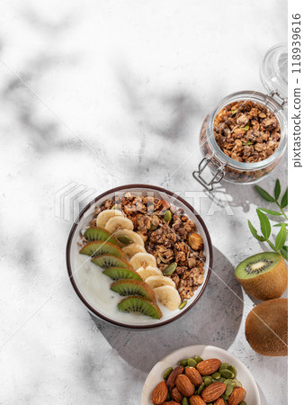 Muesli with yogurt, banana and kiwi on a light  background with shadows. 118939616