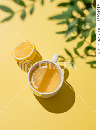 Herbal tea with lemon in a white cup on a yellow background with citrus fruit. Herbal tea with lemon in a white cup on a yellow background with citrus fruit. 118939619