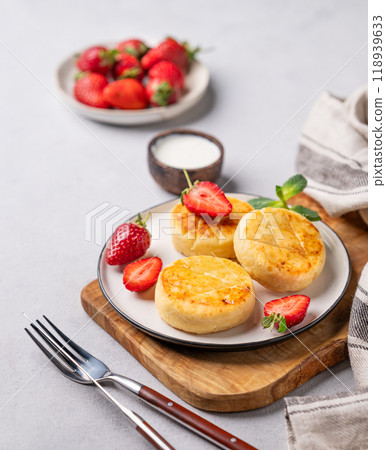 Cottage cheese, cheesecakes or syrniki with strawberries and mint leaves on a cutting board Cottage cheese, cheesecakes or syrniki with strawberries and mint leaves on a cutting board 118939633