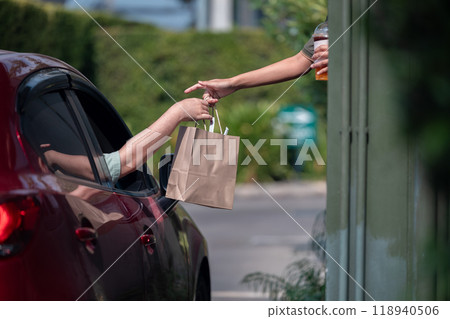 Hand Man in car receiving coffee in drive thru fast food restaurant. Staff serving takeaway order for driver in delivery window. Drive through and takeaway for buy fast food for protect covid19. 118940506