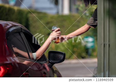 Hand Man in car receiving coffee in drive thru fast food restaurant. Staff serving takeaway order for driver in delivery window. Drive through and takeaway for buy fast food for protect covid19. 118940509