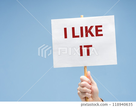 A hand holding a placard with the phrase I LIKE IT against light blue background 118940635