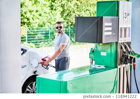 Portrait of man refueling car gas tank with gasoline. Confident driver filling full gas tank for a long road. Male adult refueling car on background of petrol station. 118941222