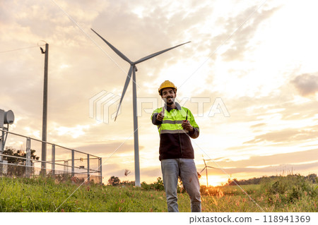 Professional Man Maintenance engineers working in wind turbine farm at sunset.  Engineer Man standing among Wind Energy Turbine. 118941369