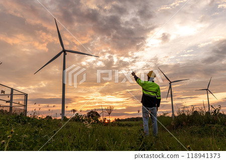 Professional Man Maintenance engineers working in wind turbine farm at sunset.  Engineer Man standing among Wind Energy Turbine. 118941373