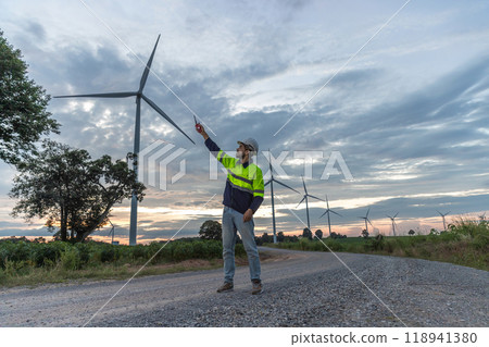 Professional Man Maintenance engineers working in wind turbine farm at sunset.  Engineer Man standing among Wind Energy Turbine. 118941380