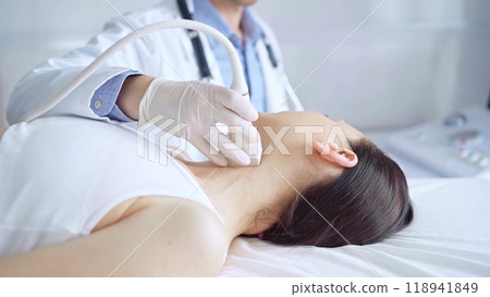 Doctor man is using ultrasound equipment on neck of female patient lying down for a medical examination. Medicine and science Doctor man is using ultrasound equipment on neck of female patient lying down for a medical examination. Medicine and science 118941849