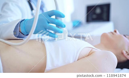 Doctor man, wearing blue medical gloves, is using ultrasound machine to examine internal organs of a patient woman, close up vie. Female mammary gland health. Medicine Doctor man, wearing blue medical gloves, is using ultrasound machine to examine internal organs of a patient woman, close up vie. Female mammary gland health. Medicine 118941874