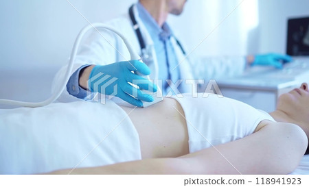 Doctor man wearing a blue medical gloves using an ultrasound equipment on a female patient lying down in clinic cabinet. Medicine concept 118941923