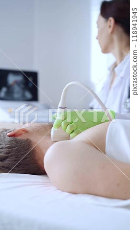 Doctor woman with green medical gloves performing neck ultrasound exam on male patient. Thyroid gland examination. Medicine concept Doctor woman with green medical gloves performing neck ultrasound exam on male patient. Thyroid gland examination. Medicine concept 118941945