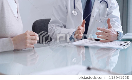 Doctor consulting patient. Male physician is gesturing above a clipboard while talking with a woman in a clinic, close up. Medicine concept Doctor consulting patient. Male physician is gesturing above a clipboard while talking with a woman in a clinic, close up. Medicine concept 118941968