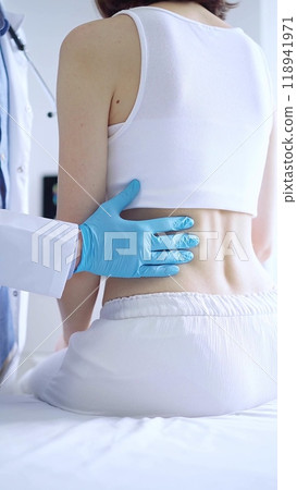 Doctor and patient. Physician wearing blue gloves examining back of female patient in clinic. Orthopedics in medicine 118941971