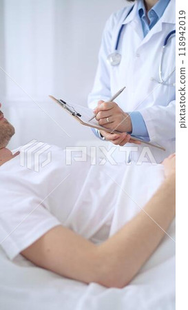 Female doctor writing medical report of patient lying in bed in hospital Female doctor writing medical report of patient lying in bed in hospital 118942019