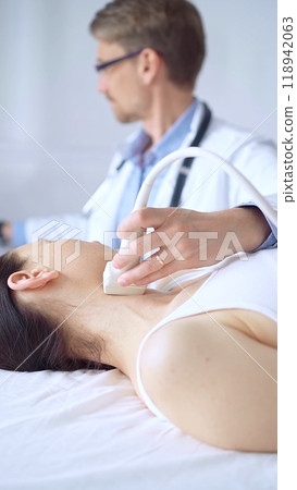 Doctor man using ultrasound equipment on the neck of a patient woman, lying for examination. Medicine concept Doctor man using ultrasound equipment on the neck of a patient woman, lying for examination. Medicine concept 118942063