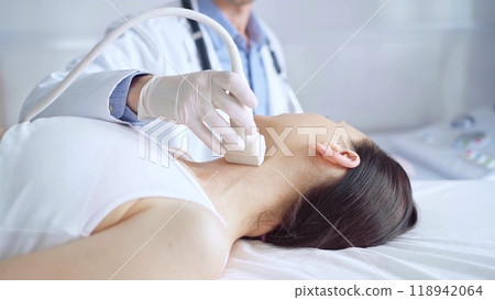 Doctor man is using ultrasound equipment on neck of female patient lying down for a medical examination. Medicine and science Doctor man is using ultrasound equipment on neck of female patient lying down for a medical examination. Medicine and science 118942064