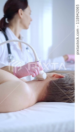 Doctor woman with pink medical gloves performing neck ultrasound exam on male patient. Thyroid gland examination. Medicine concept Doctor woman with pink medical gloves performing neck ultrasound exam on male patient. Thyroid gland examination. Medicine concept 118942065